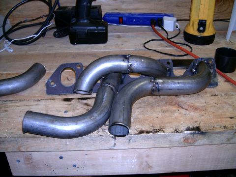 1978 Ford Mustang II - Custom exhaust headers and a gasket sit on a wooden workbench, likely awaiting installation.
