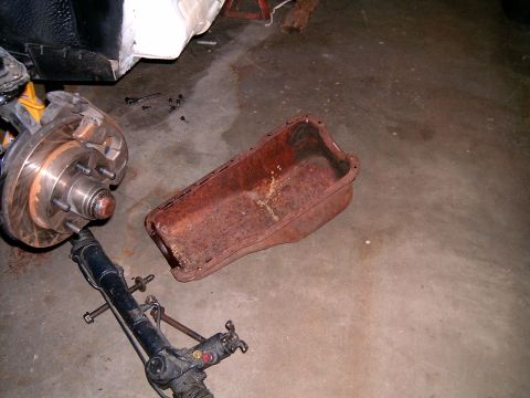 1978 Ford Mustang II - Disassembled car parts, including a rusty oil pan and front suspension, lie on a concrete floor.