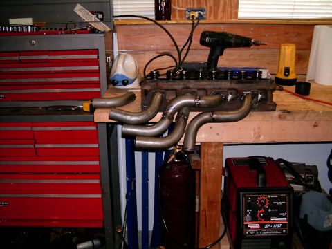 1978 Ford Mustang II - Custom exhaust headers are laid out next to an engine block, with tools and welding equipment nearby.