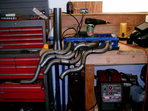 1978 Ford Mustang II - Custom exhaust headers are shown mounted to a blue engine block, with a welding machine and tools in the background.
