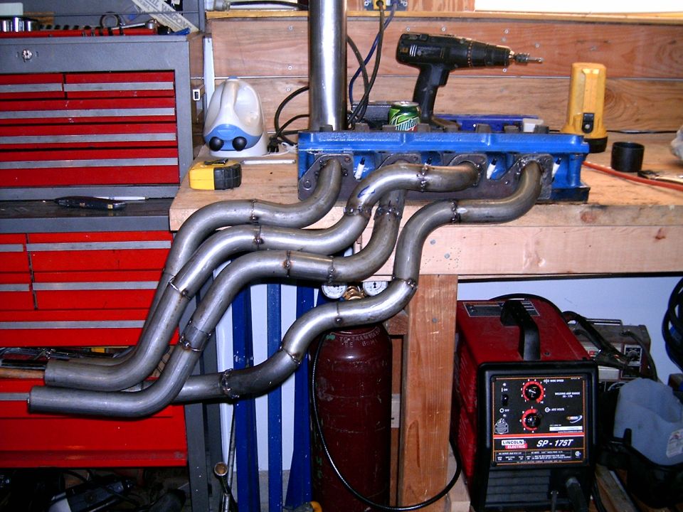 custom exhaust headers on a workbench next to a welding machine and toolbox