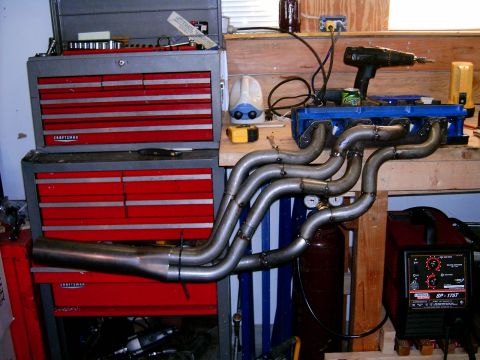 1978 Ford Mustang II - Custom exhaust headers are shown on a workbench, surrounded by tools and welding equipment, suggesting a custom automotive project.