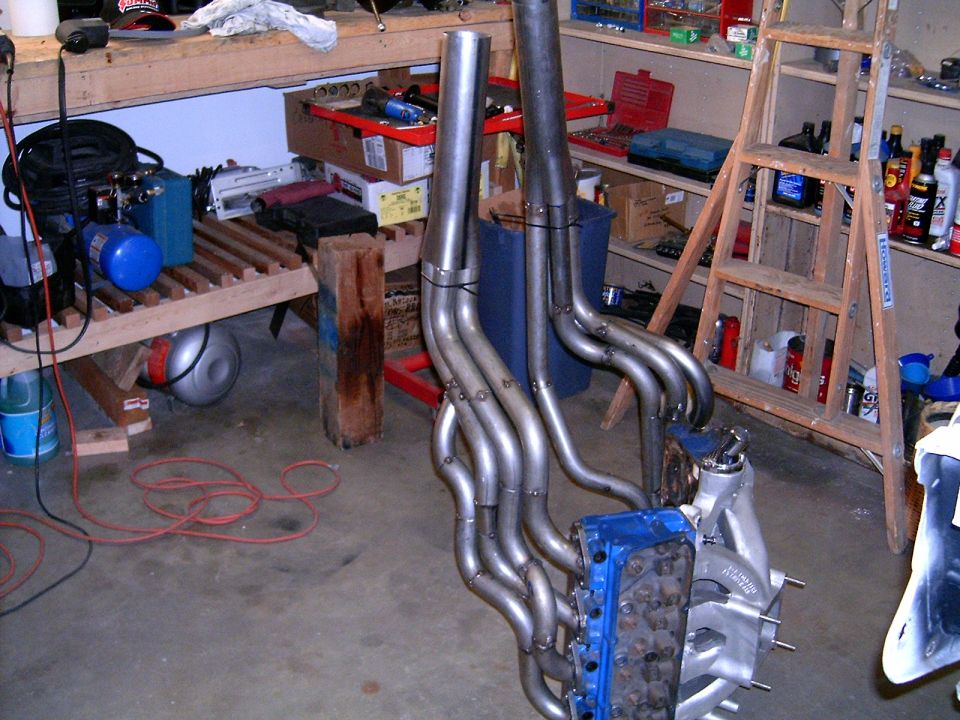 Engine block with custom headers attached, sitting on a garage floor