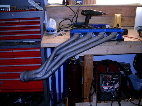 1978 Ford Mustang II - Exhaust headers sit on a workbench next to a drill and welding equipment, suggesting a repair or customization project.