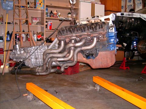 1978 Ford Mustang II - A V8 engine and transmission assembly, fitted with custom exhaust headers, is suspended by a chain hoist in a garage setting.