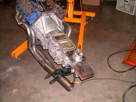 1978 Ford Mustang II - Engine and transmission assembly with custom headers is supported by an orange engine stand in a garage setting.