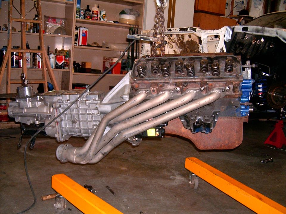 Engine and transmission assembly with custom headers, being worked on in a garage