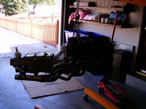 1978 Ford Mustang II - Engine and transmission assembly with custom headers, suspended by a chain hoist in a garage.