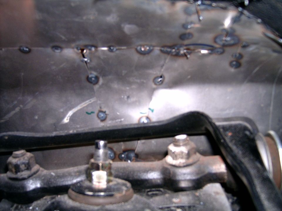 Close-up of a crudely welded metal panel with visible bolts and nuts below