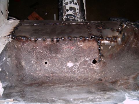 1978 Ford Mustang II - Close-up view of a vehicle's floor pan undergoing repair with fresh welds and two drilled holes.