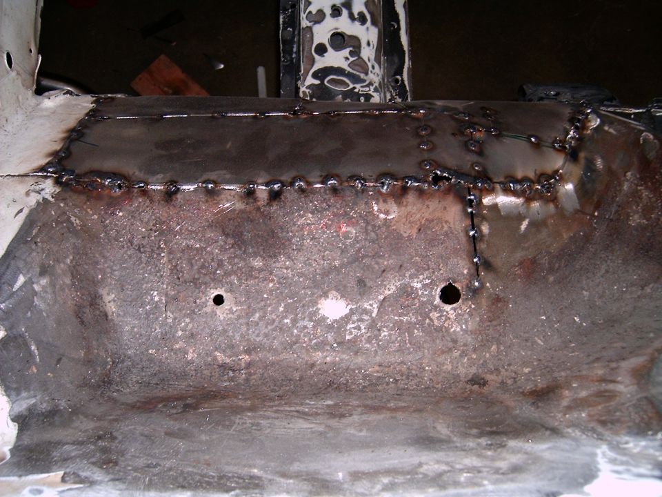 Welded floor pan repair with visible stitch welds and two circular holes
