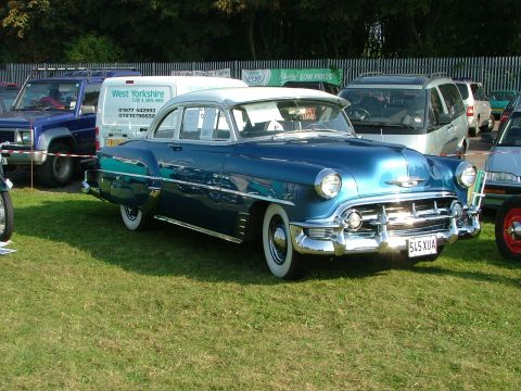 1988 Ford Sport - A vintage blue sedan is parked on a grassy field next to other vehicles and a white van.