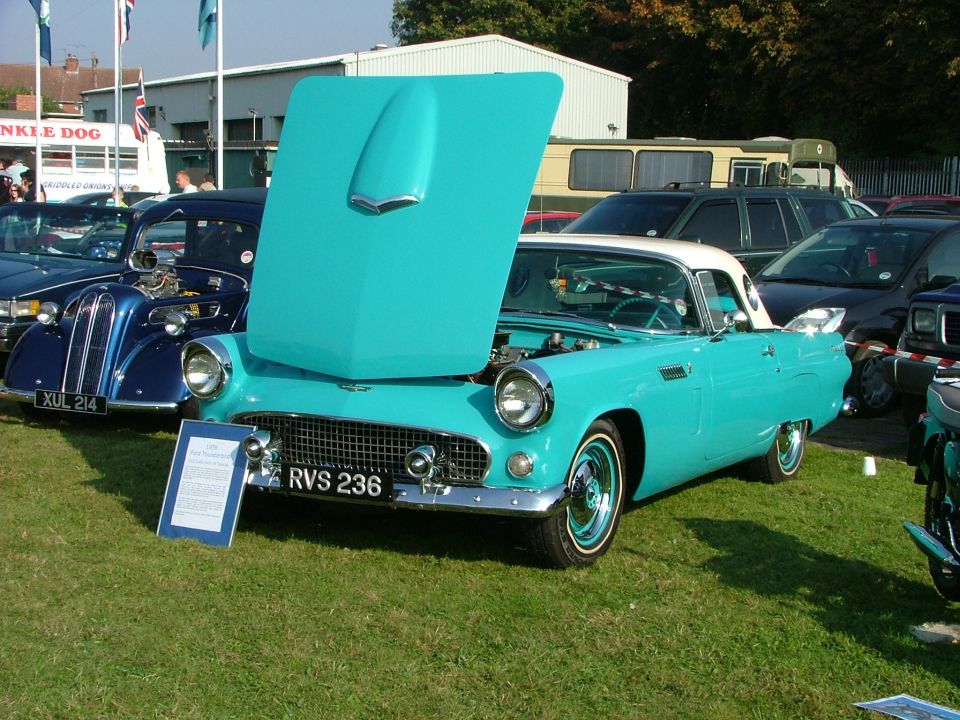 Turquoise and white convertible with hood open, parked on grass. License plate RVS 236