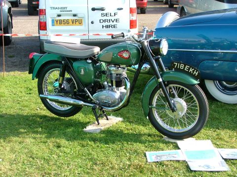 1988 Ford Sport - A green motorcycle is parked on grass, with a white van and a blue car in the background.