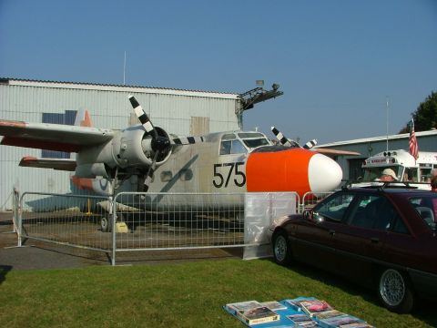 1988 Ford Sport - A maroon sedan is parked next to a twin-engine airplane on display at an outdoor event.