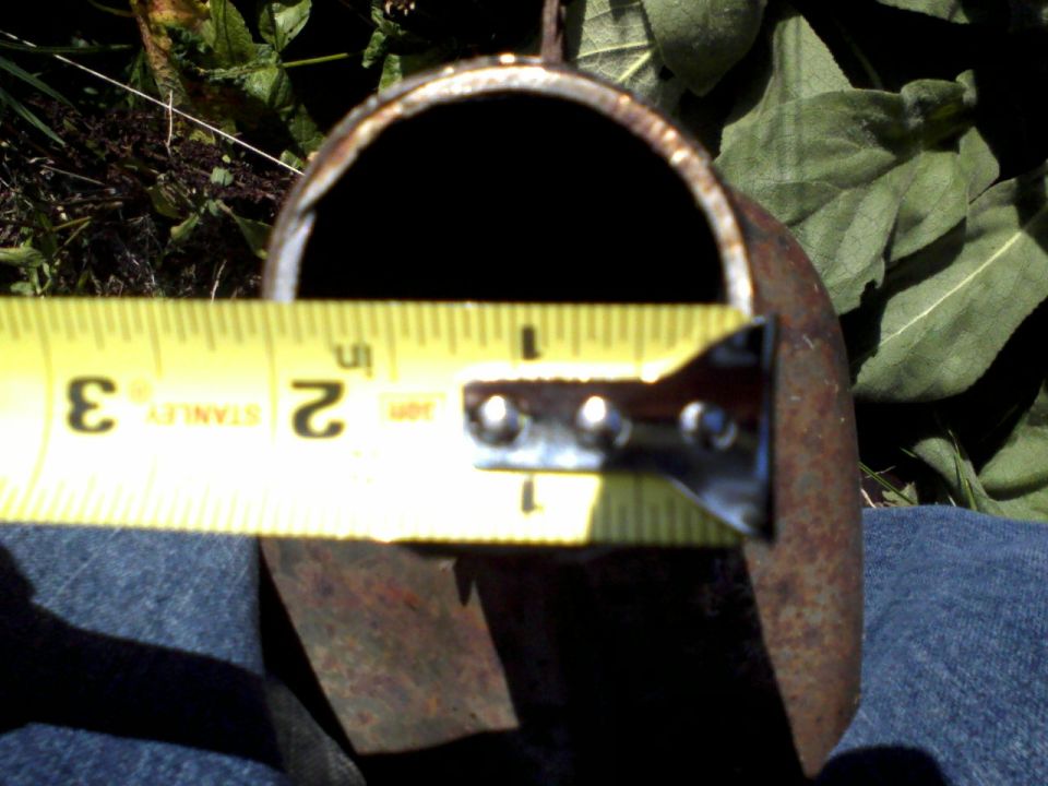 Rusty curved metal part measured with a yellow Stanley tape measure outdoors