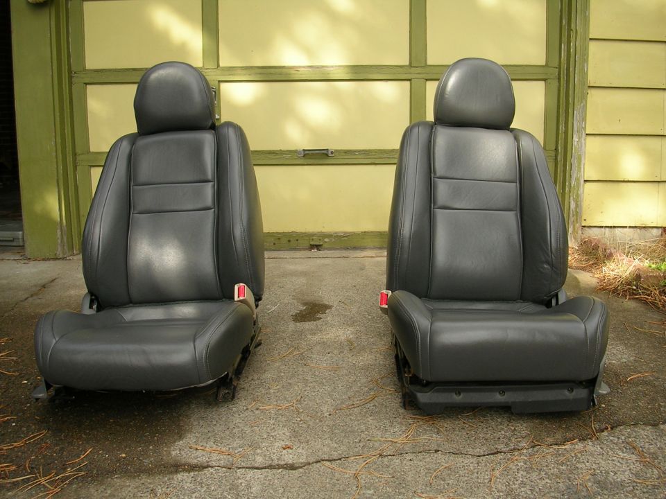 Two black leather car seats with red seatbelt buckles, viewed from the front