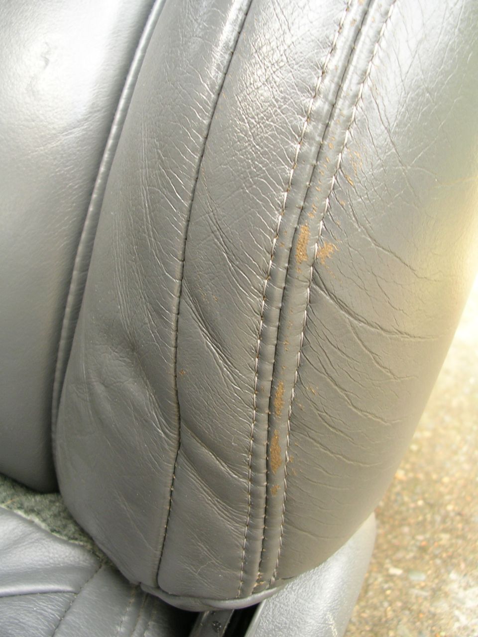 Close-up of gray leather car seat with visible stitching and some rust-colored stains