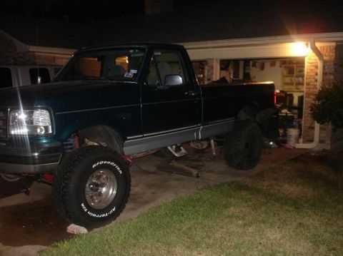 1996 Ford F-150 - A lifted 1996 Ford F-150 pickup truck is parked in a driveway at night, with its front end visible.