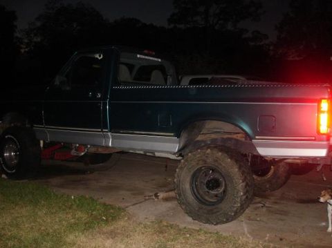 1996 Ford F-150 - Side view of a lifted dark green pickup truck with off-road tires, parked at night.