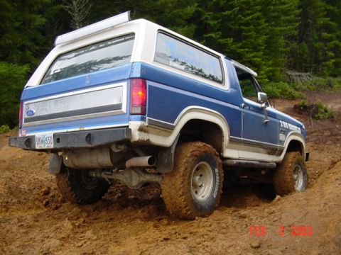 1985 Ford Bronco - This blue and white Ford Bronco is seen from a 3/4 front angle on a muddy trail.
