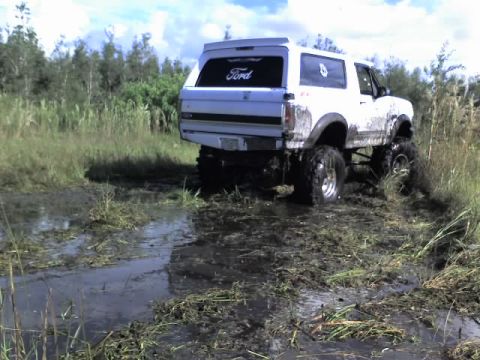 1995 Ford Bronco - A white Ford Bronco navigates a muddy off-road trail.