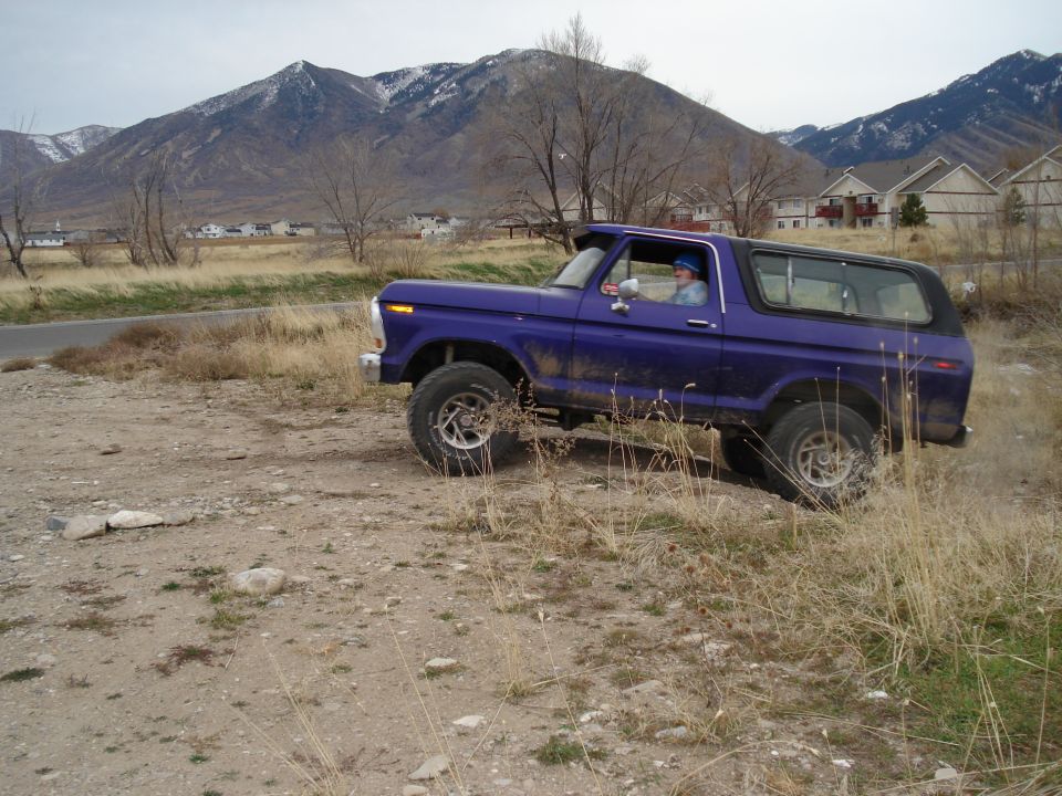 Purple 1978 Ford Bronco driving off-road with mountains in background