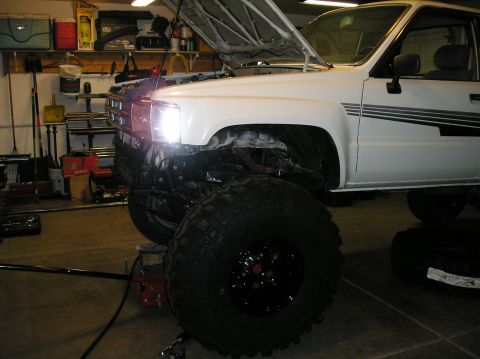 1986 Toyota Hilux - White pickup truck with hood open, lifted suspension, and large off-road tires in a garage.