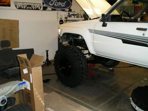 1986 Toyota Hilux - A white 1986 Toyota Hilux is shown with its hood open and massive off-road tires, suggesting modifications or repairs.