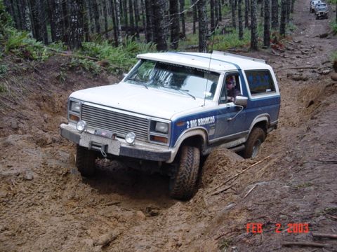 1985 Ford Bronco - Ford Bronco navigating a muddy off-road trail with another vehicle in the background.