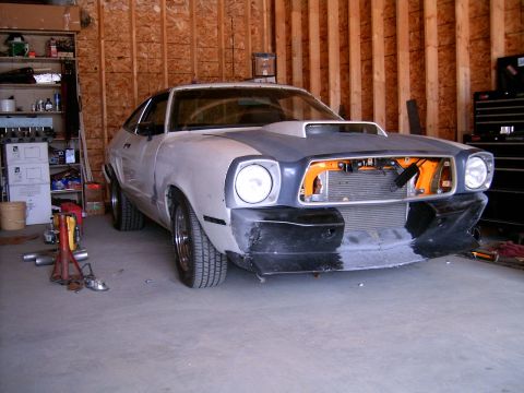 1978 Ford Mustang II - A 1978 Ford Mustang II is parked in a garage, showing its front end with the hood up and the grille area exposed.