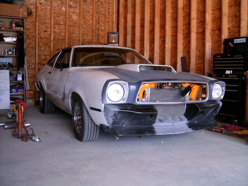White and grey Ford Mustang II undergoing restoration, front view, hood scoop, missing grille components