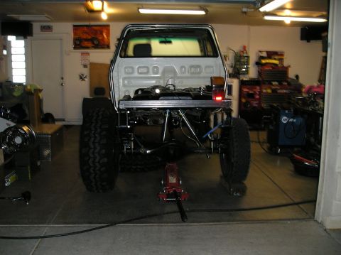 1986 Toyota Hilux - Rear view of a white pickup truck chassis with oversized tires, undergoing work in a garage setting.