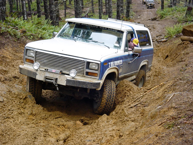 White and blue Ford Bronco with winch on front bumper navigating a muddy trail