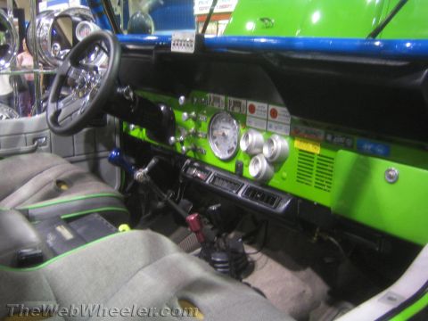 1990 Ford Bronco - Interior of a green off-road vehicle showing a black steering wheel, green-trimmed dash with gauges and a cloth bucket seat.
