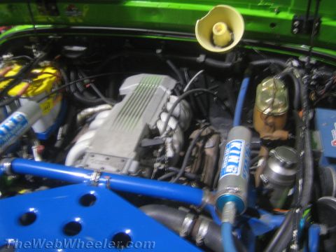 1990 Ford Bronco - Open engine bay of a green vehicle showing blue KING coilover reservoirs, an aluminum intake plenum and assorted hoses.