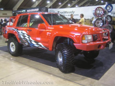 1990 Ford Bronco - red lifted SUV with tribal flame graphics on big mud tires displayed in front of a TrailReady beadlocks booth.