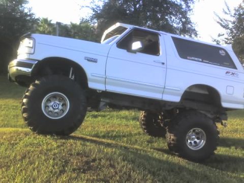 1995 Ford Bronco - Modified white Ford Bronco with custom suspension and large off-road tires sits on a grassy incline.
