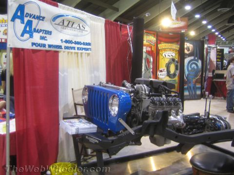 1990 Ford Bronco - Advance Adapters Atlas transfer-case booth featuring a blue Jeep front clip with an exposed engine on a bare frame.
