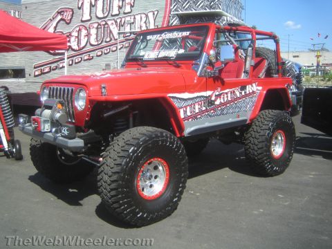 1990 Ford Bronco - red lifted Jeep Wrangler with Tuff Country diamond-plate graphics, winch bumper and mud tires parked outside a Tuff Country building.