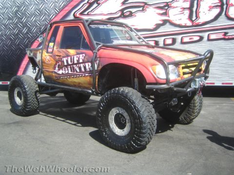 1990 Ford Bronco - Toyota pickup-bodied rock buggy with a flame wrap, Tuff Country graphics and large mud tires parked on pavement outdoors.