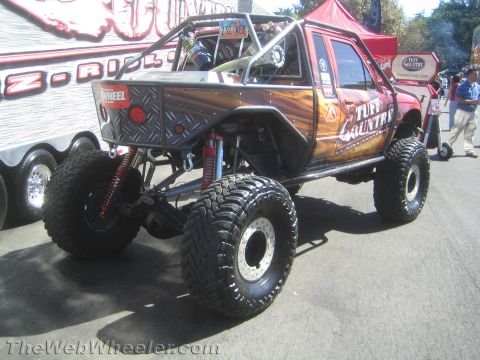1990 Ford Bronco - Rear three-quarter view of a flame-wrapped Toyota rock buggy with red coilover shocks, Tuff Country graphics and large mud tires.