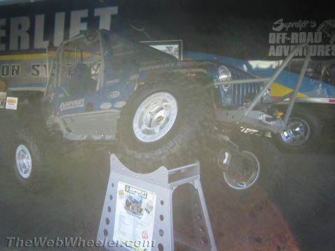 1990 Ford Bronco - blue tube-chassis Jeep-style rig sits on a Superlift off-road suspension display banner at an indoor show.