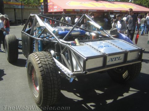 1990 Ford Bronco - skeletal tube-frame off-road race truck with ATL fuel cells sits on display in a crowded outdoor pit area.