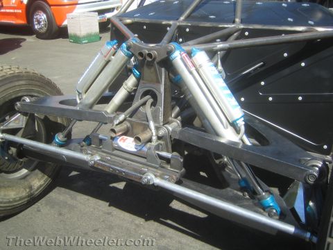 1990 Ford Bronco - rear of a tube-frame off-road buggy reveals its trailing-arm suspension and multiple blue-bodied shock absorbers.