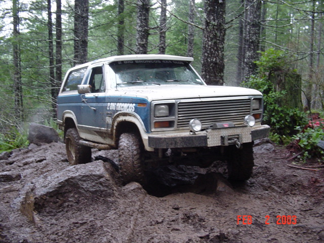 Ford Bronco driving over rocks and mud in a forest