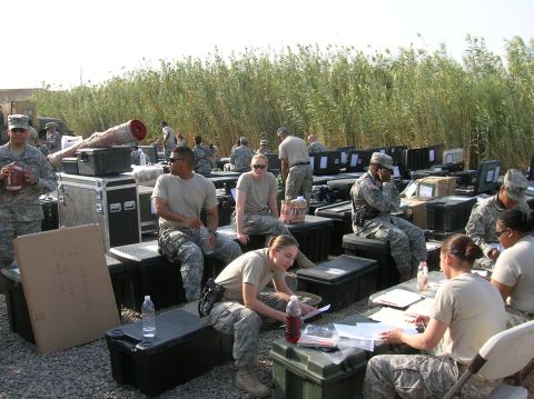 1996 Ford Bronco - A group of soldiers are seated around various pieces of equipment, with tall reeds visible in the background.