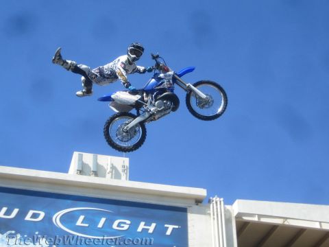 1990 Ford Bronco - motocross rider kicks his legs out behind a blue dirt bike mid-jump above a Bud Light stadium sign.