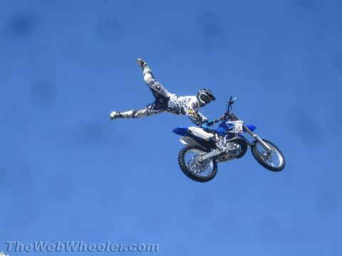 1990 Ford Bronco - freestyle rider stretches into a superman pose off a blue dirt bike against a deep blue sky.