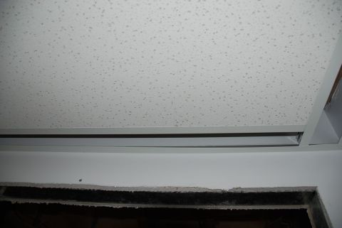 1996 Ford Bronco - A view of a drop ceiling with acoustic tiles and a metal grid, above a damaged wall opening.